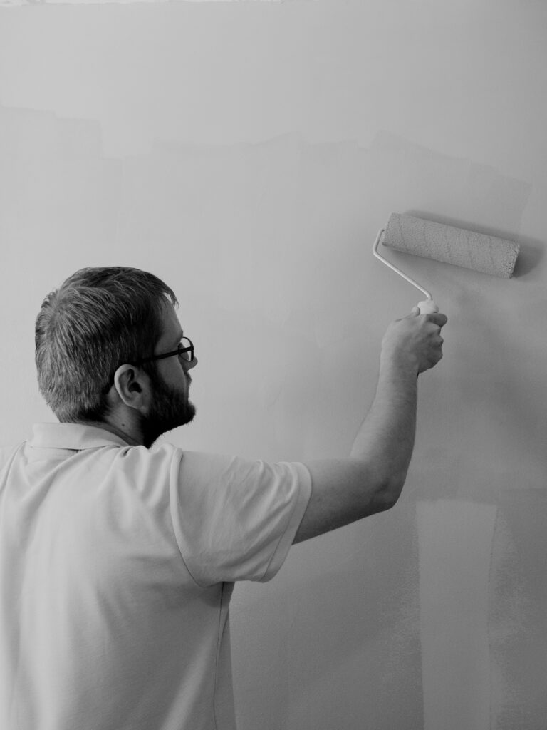 A man painting a wall using a roller in a black and white composition.